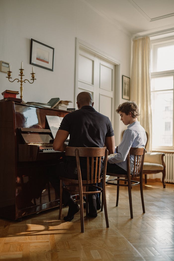 Man teaching piano to a student in a bright room with natural light.